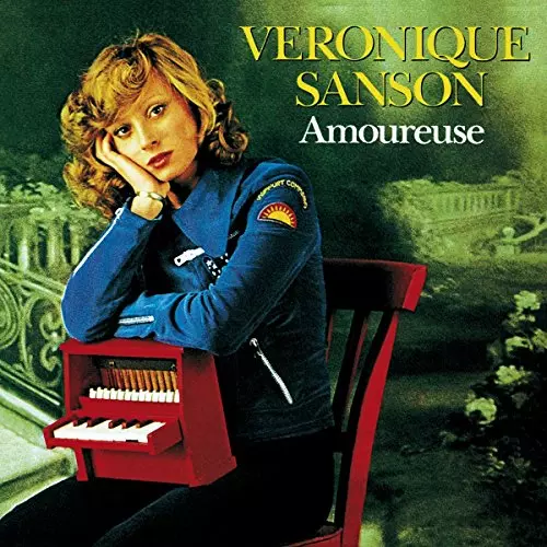 Véronique Sanson assise, à la tête posée sur une main, et mini piano sur les jambes