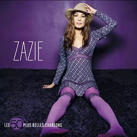 Photo entière fond violet de Zazie en chapeau assise sur un tapis