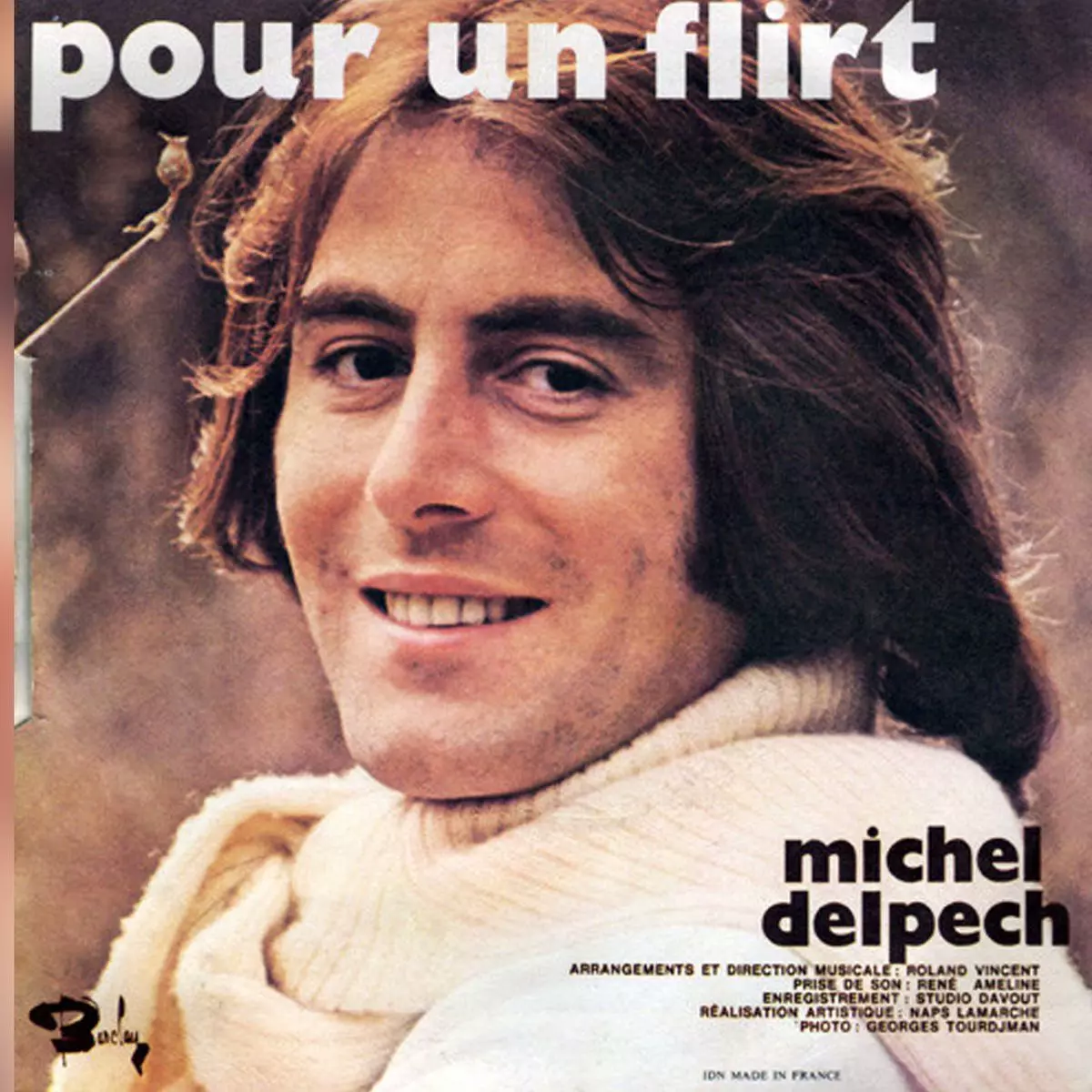 Gros plan sur Michel Delpech dans un champ, souriant