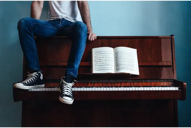 Une personne est entrain de jouer du piano, elle à en face d'elle un cahier rempli de note de musique 