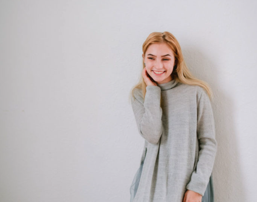 jeunne fille souriante posant devant un fond gris 